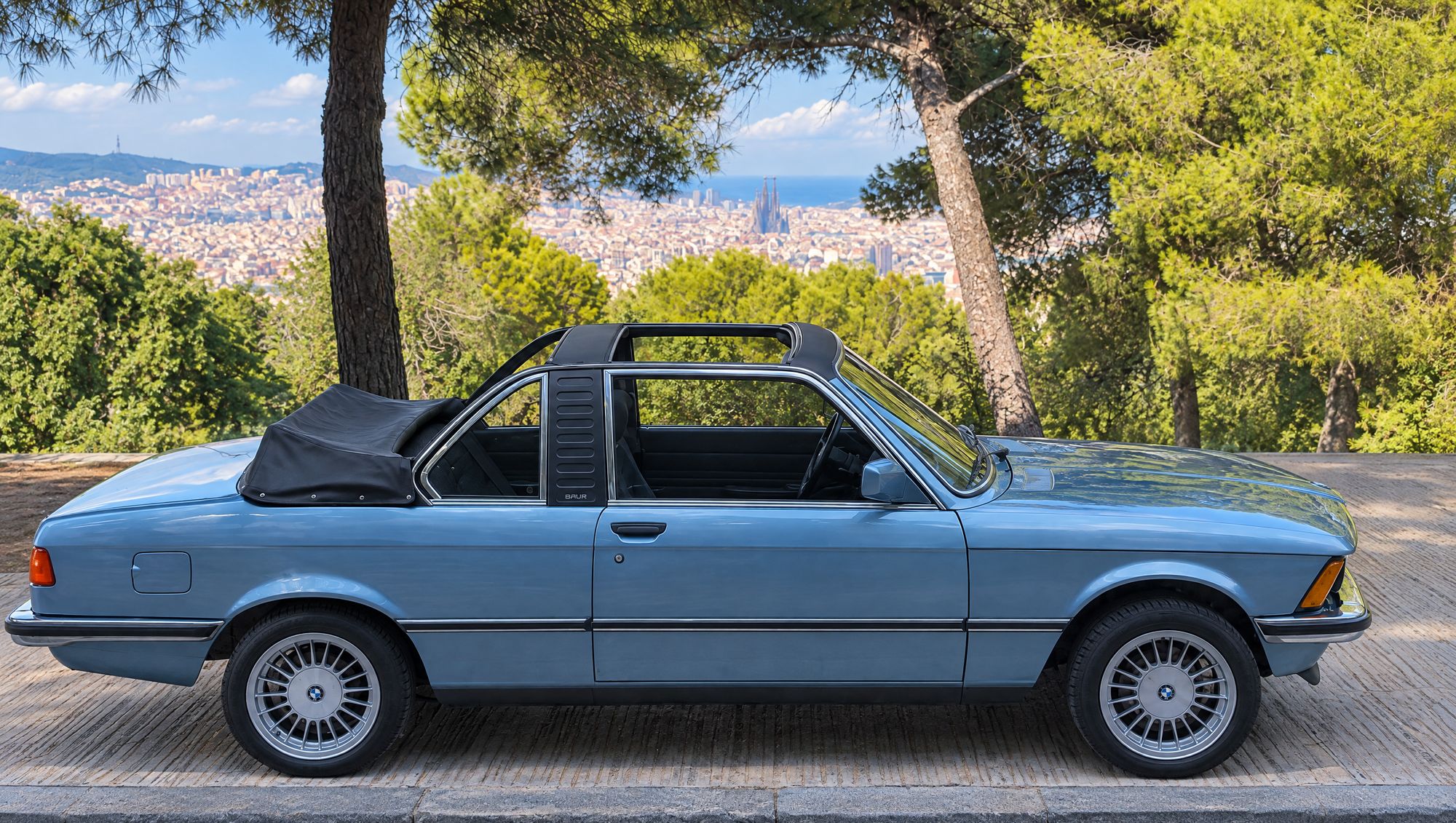 BMW E21 Baur TopCabriolet in Stratosblau, roof open, parked on Montjuïc with Barcelona behind